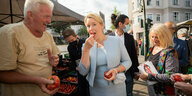 Franziska Giffey isst eine Tomate an einem Marktstand