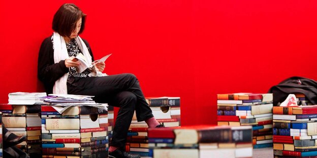 Eine Frau sitzt vor einer roten Wand und blättert in einem Buch