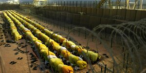 Menschen in gelben Gewändern knieen auf dem Boden eines Gefangenenlagers