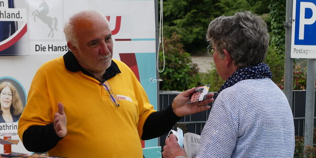 Ein Mann mit weißen Haaren und gelbem CDU Shirt spricht gestikulierend mit einer Frau: Necdet Savural