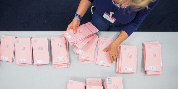 Zwei Hände sortieren rosafarbene Briefwahlumschläge.