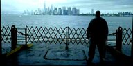 Filmstill: En Mann schaut mit dem Rücken zur Kamera über das Wasser in Richtung Manhatten, dorthin, wo das WTC stand