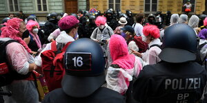 Demonstranten mit pinkfarbenen Perücken und Mützen umgeben von Polizisten in einer Wohnstrasse