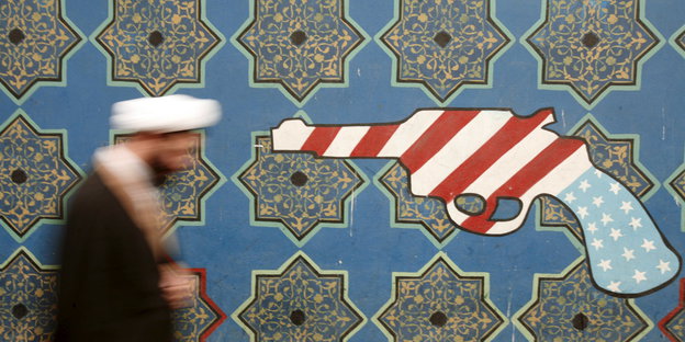 Ein Iraner läuft an einer Mauer entlang, an der ein Symbol einer amerikanischen Waffe klebt