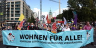 Menschen auf einer Mietendemo, im Vordergrund ein Plakat mit der Aufschrift "Wohnen für alle!"