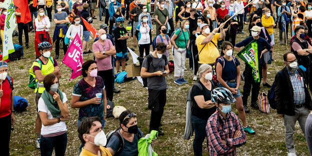 Menschen mit Mund-Nasen-Masken stehen auf einer Wiese und gucken in die gleiche Richtung