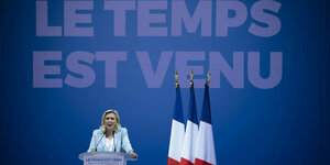 Eine Frau in einem Anzug spricht an einem Rednerpult. Neben stehen drei Fahnen Frankreichs. Hinter ihr prangt der Schriftzug: Le temps est venu