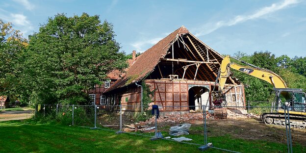 Ein Abrissbagger steht vor dem zerstörten Dach des Wünninghofs in Ostenholz.