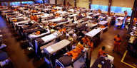 Häftlinge liegen auf Betten in einer Sporthalle
