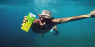 Promofoto: Ein Mann mit Hut und einer Tüte Eistee schwimmt unter Wasser