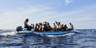 17 Menschen sitzen eng gedrängt in einem Schlauchboot auf dem offenen Meer