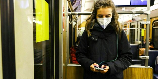 Eine Frau trägt eine Maske in der U-Bahn und schaut auf ihr Handy