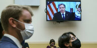 Zwei MÄnner mit Maske, im Hintergrund ist der US-Außenminister Antony Blinken auf einem Bildschirm zu sehen