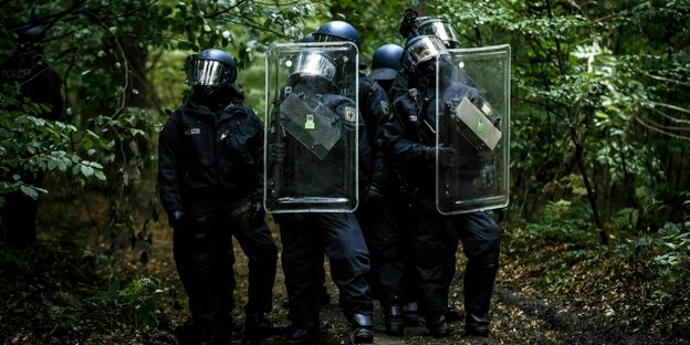 Polizisten in voller Schutzmontur mit Helm und Schild gehen durch den Hambacher Forst