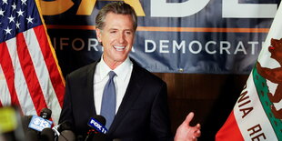 Gavin Newsom am Rednerpult zwischen Flaggen