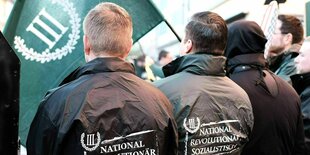 Zwei Männer halten eine Flagge der Partei III. Weg und tragen eine Jacke mit der Aufschrift "National, Revolutionär, Sozialistisch"