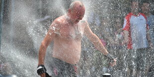 Ein Mensch lässt sich von einem Hydranten nass spritzen