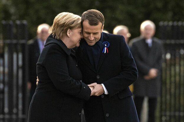 Angela Merkel und Emmanuel Macron schütteln sich die Hände und stecken die Köpfe zusammen