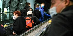 Menschen tragen Maske auf einer Rolltreppe im Flughafen Frankfurt