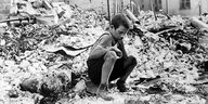Ein Junge sitzt auf einem Schutthaufen in einer zerstörten Stadt