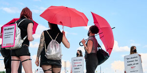 Knapp bekleidete Frauen mit roten Schirmen und Protestplakaten