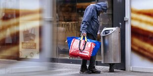 Mann mit Anorak sucht in Papierkorb nach Pfandflaschen