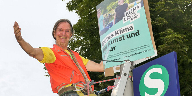 Ein Mensch hängt ein Wahlplakat an einer Laterne auf