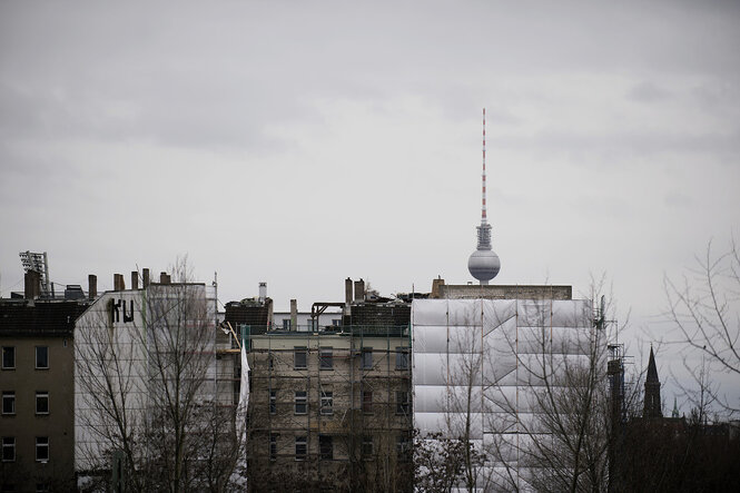 Häuserzeile mit eingerüsteten Fassaden, im Hintergrund sieht man den Berliner fernsehturm