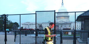 Ein Polizist vor dem umzäunten Kapitol in Washington schaut auf sein Smartphone