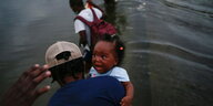 Haitianer auf der Flucht durchqueren einen Fluß. Ein Mann hält ein verängstigtes Baby auf dem Arm