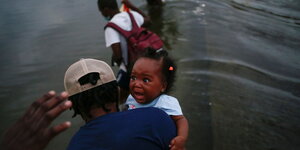 Haitianer auf der Flucht durchqueren einen Fluß. Ein Mann hält ein verängstigtes Baby auf dem Arm