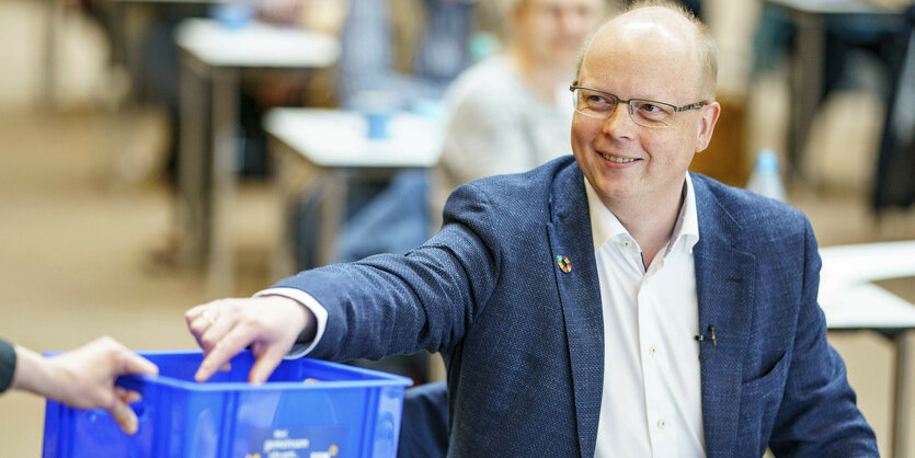 Stefan Seidler sitzt an einem Tisch und gibt eine Abstimmungskärtchen in eine Kiste