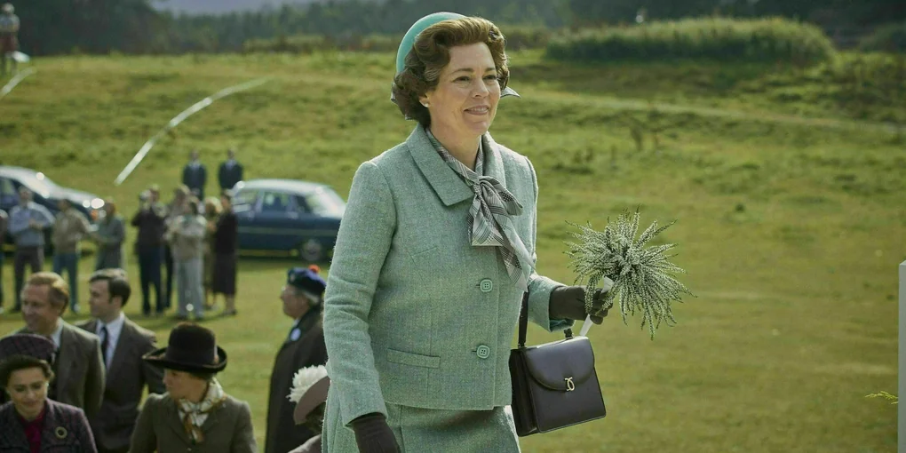 Eine Frau in einem blauen Kostüm gekleidet trägt einen schwarze Handtasche und einen Blumenstrauß