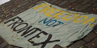 Ein Stoffbanner mit der Aufschrift freedom not frontex liegt auf dem Straßenbelag