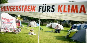 Hungerstreik fürs Klima steht auf einem Sonnenschirm, dahinter Zelte