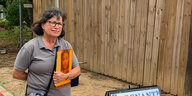 Eine Frau mit einem Foto steht vor einem Holzzaun