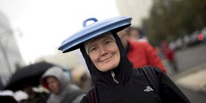 Eine Frau trägt einen Topfdeckel auf dem Kopf