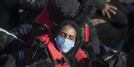 Eine Frau mit Rettungsweste und Mundschutz hält ihre Augen geschlossen