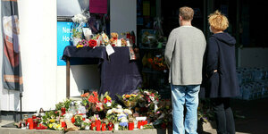 Zwei Menschen stehen vor dem Tatort in Idar-Oberstein - rundherum liegen Blumen, Kerzen und Botschaften.