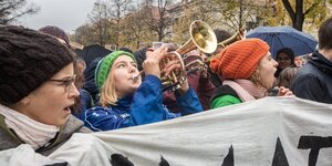 Junge Menschen demonstrieren. Sie tragen ein Transparent, einer spielt trompete