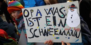 Ein Kind hält ein Plakat mit der Aufschrift "Opa was ist ein Schneemann"