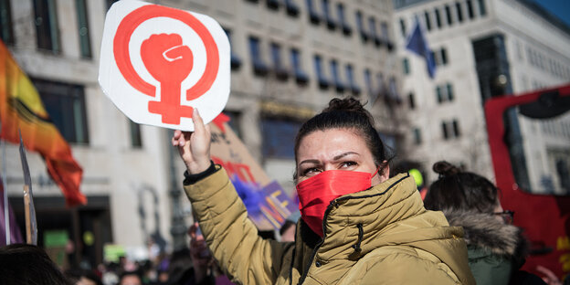 Eine Frau hält ein Plakat mit einem Frauenzeichen und einer Faust in die Höhe