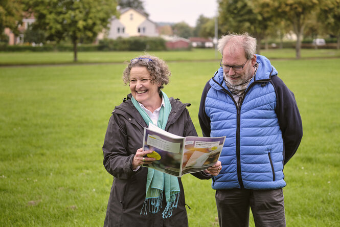 Eine Frau hält eine Zeitung und lacht, neben ihr steht Klaus Winkel