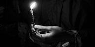 Schwarzweiß-Aufnahme: eine Hand hält eine angezündete Kerze