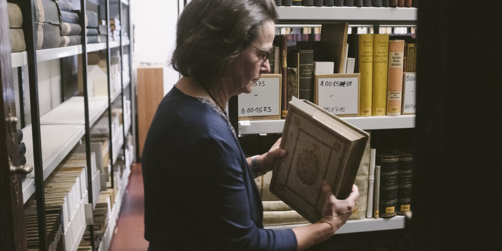 Eine Frau steht zwischen vollen Regalen in einer Bibliothek