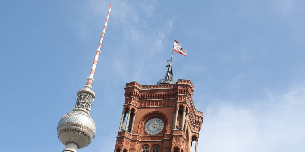 Blick in den Himmel. Der Fernsehturm mit seiner Kugel und das Rote Rathhaus ragen in den blauen Himmel. Nur ein paar weiße Wolken sind dort.