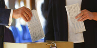 Zwei Hände halten einen Stimmzettel, bei dem einen ist das Ergebnis erkennbar