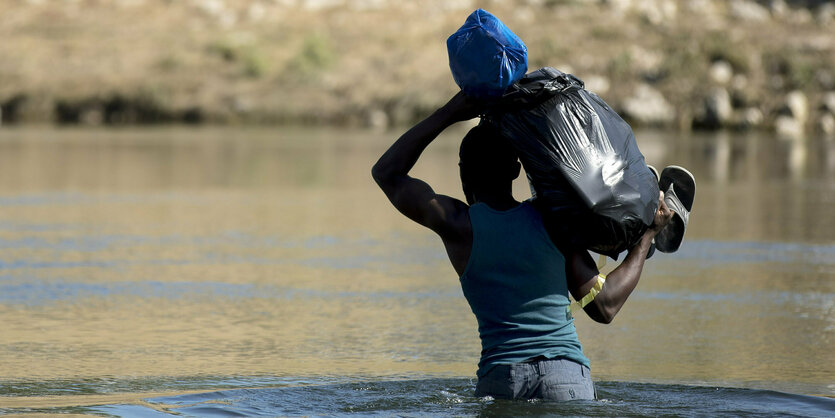 Mensch mit Plastiksack geht durch hüfthohes Wasser