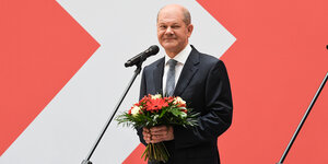 Olaf Scholz steht mit einem Blumenstrauß am Mikrofon