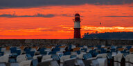Die aufgehende Sonne färbt den Himmel hinter dem Leuchtfeuer auf der Mole an der Ostsee orangerot ein.